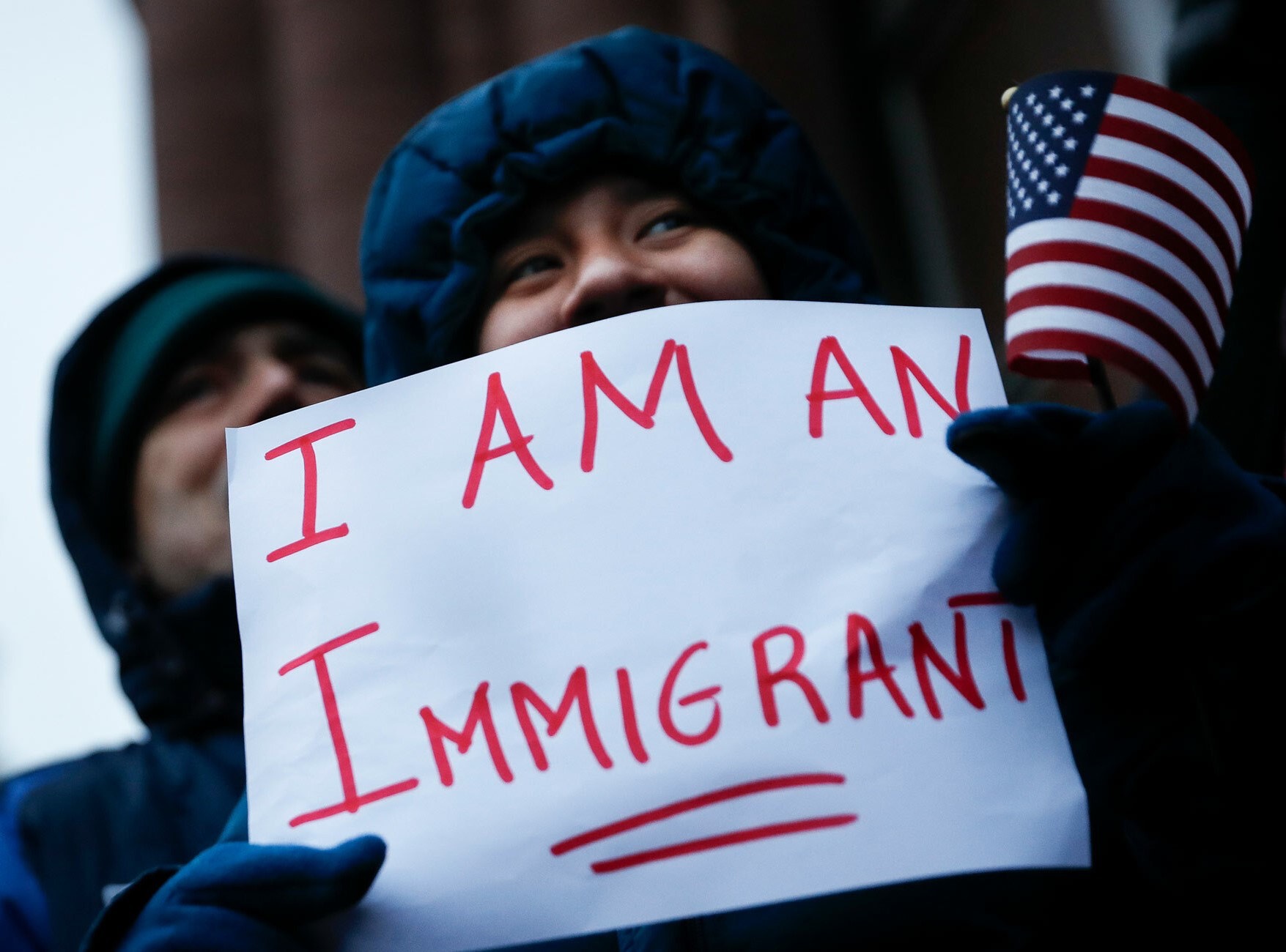 Person holding a sign saying "I am an immigrant" and an American flag